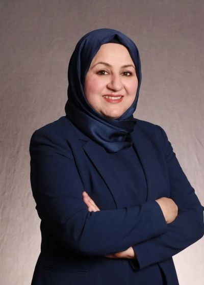 Woman smiling confidently with arms crossed, wearing navy hijab and suit.