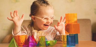 Joyful child with glasses playing with colorful translucent blocks.