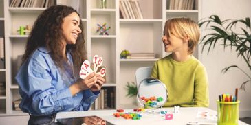 A woman and child playing an educational game with letter cards at a table.