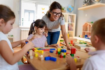 Teacher guiding children playing with colorful wooden blocks in classroom.