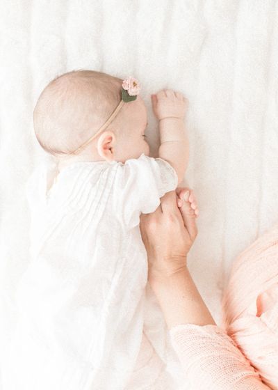 baby sleeping in bed with flower in hair holding moms hand 