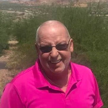 Man in a bright pink shirt smiling outdoors.