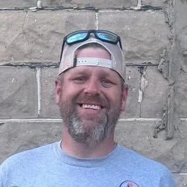 Smiling man with beard and backward cap.
