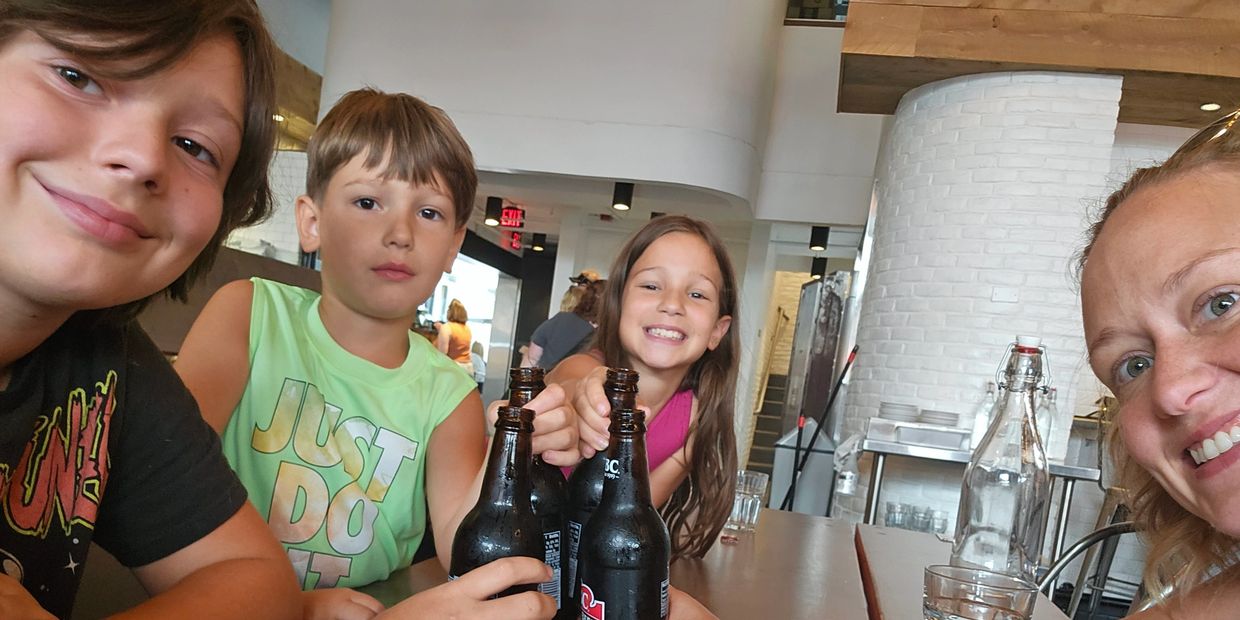 Four people smiling and holding dark bottles at a table indoors.