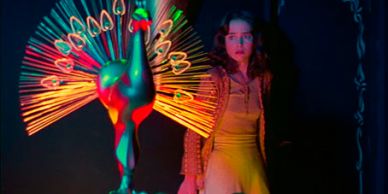 Woman illuminated by colorful light from peacock statue.