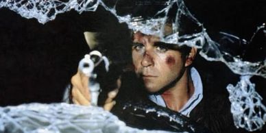 Man aiming gun through broken glass with bruised face.