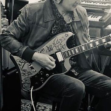 Musician playing a signed electric guitar in a studio setting.