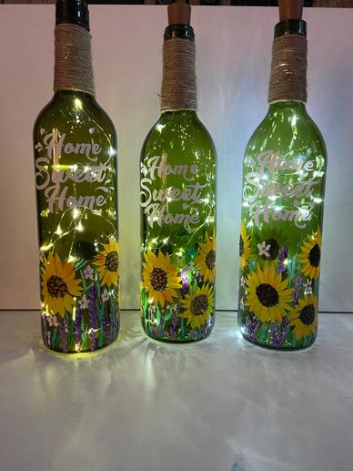 Three green bottles with sunflower designs and lights inside.