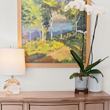 Orchid, lamp, and painting on wooden dresser.