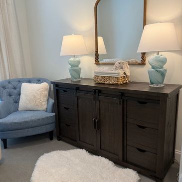 Cozy corner with a blue armchair, dark wooden dresser, and lamps.
