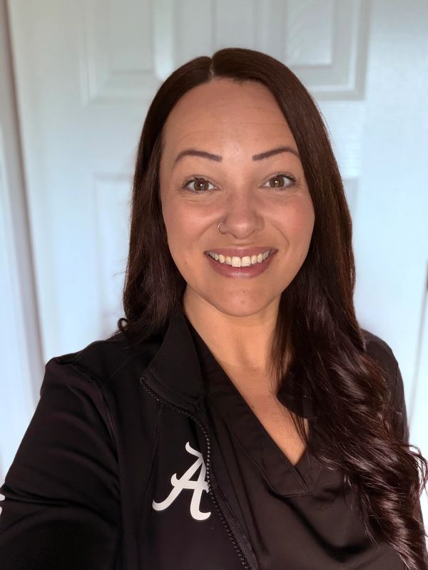 Smiling woman with long dark hair wearing a black jacket with an Alabama logo.