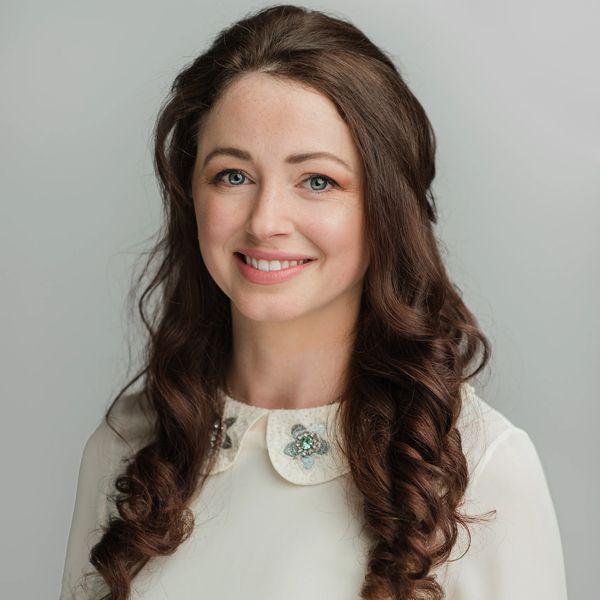 Smiling woman with curly brown hair in a white top.