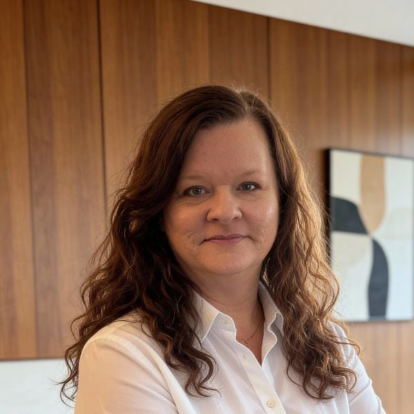 Professional woman with curly hair in a white shirt, standing confidently indoors.