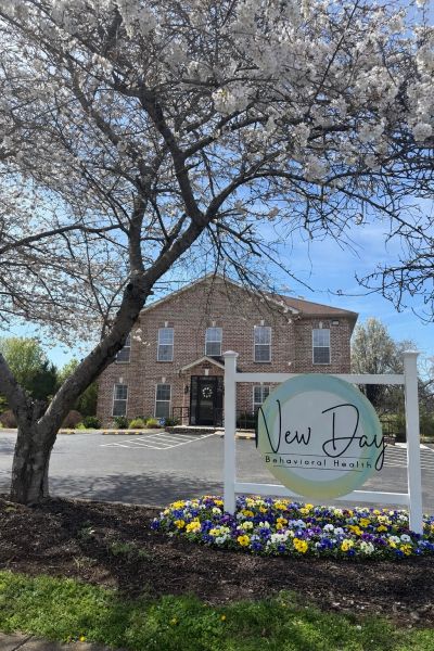 Cherry blossom tree in front of a brick building with a New Day Behavioral Health sign.