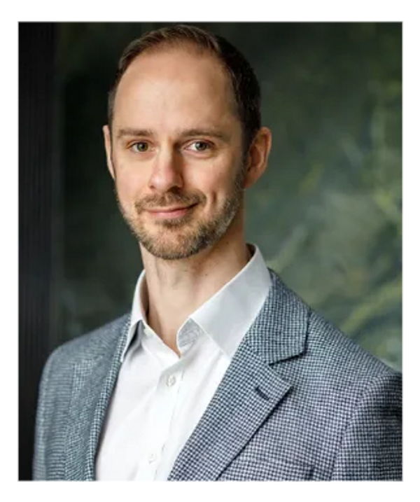 Portrait of a confident man in a gray checkered blazer and white shirt.