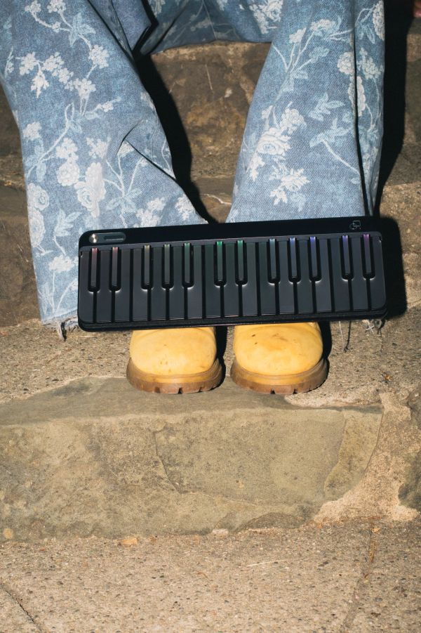 Person wearing yellow boots and floral pants holding a small electronic keyboard.