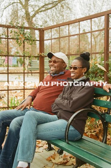 Married couple smiling together on a bench during overcast day. 