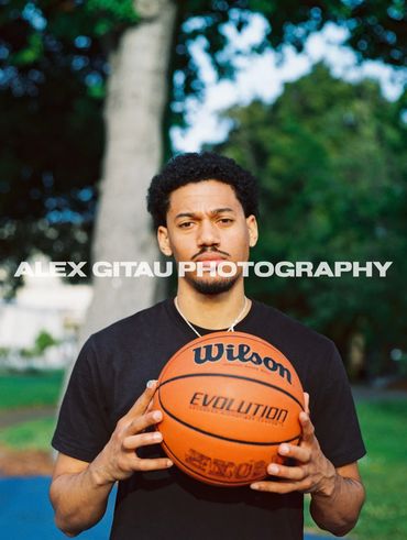 Man holding a basketball outdoors with trees in the background.
