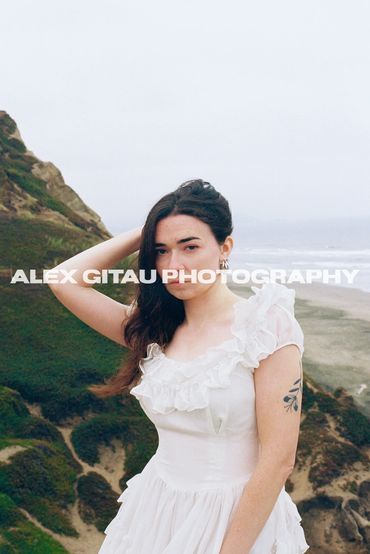 Young woman posing in front of beach cliffside on an overcast day. 