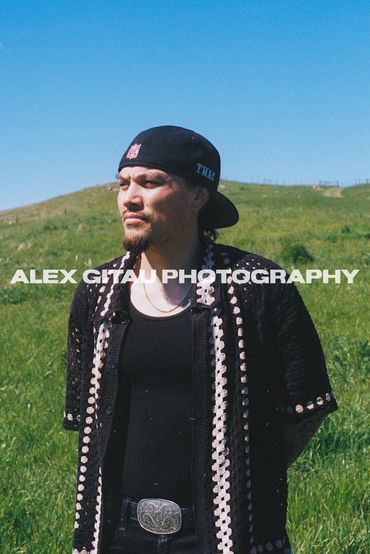 Man in black shirt posing on grassy filed in midday sunlight. 
