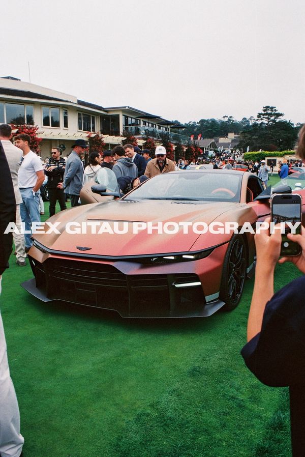 Matte brown sports car at a car show with people around.
