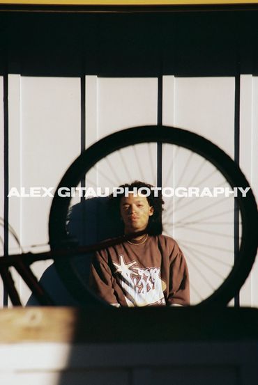 Man posing behind bicycle spokes in summertime sunset setting. 