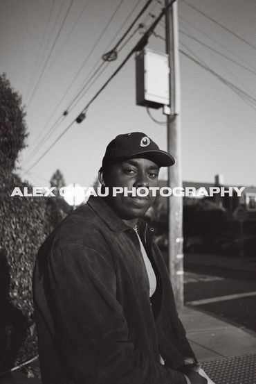 Man in a cap posing on a street corner in black and white.