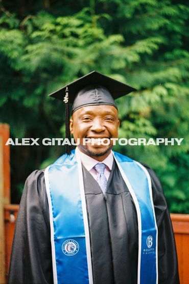 Man in graduation cap and gown posing in backyard with overcast sunlight,