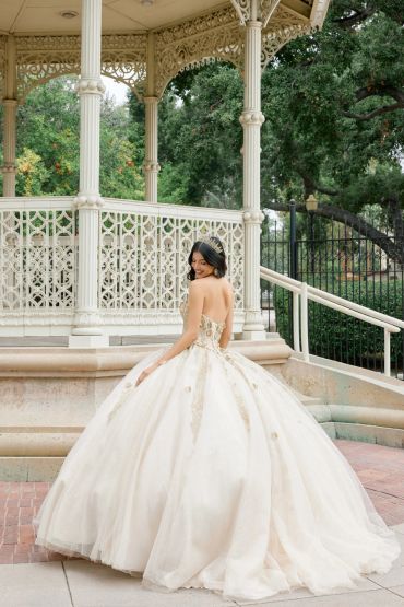 Young woman in a white ball gown standing near a gazebo.