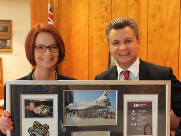 Two people holding a framed collage with space-related images.