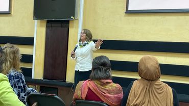 A woman speaks to an attentive audience in a classroom or seminar setting.