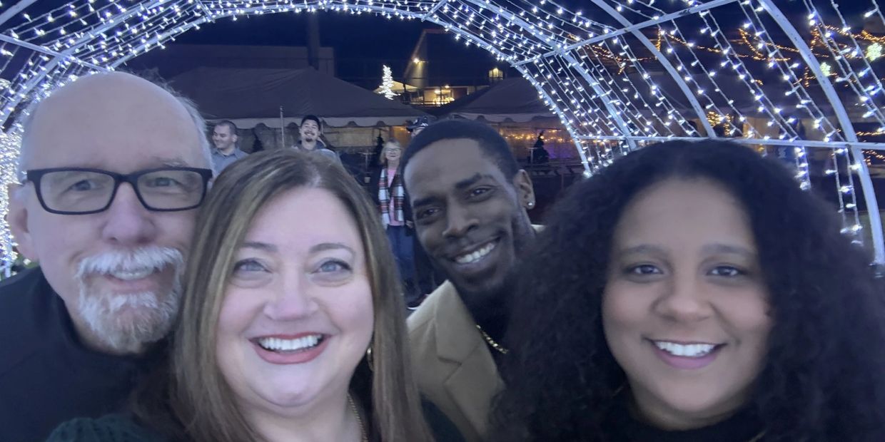 Four friends happily posing under festive lights at night.