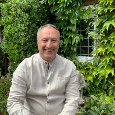 Smiling man in a light shirt sitting in a lush garden.