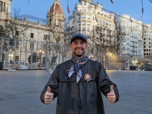 Hombre sonriente con pulgares arriba en plaza urbana.