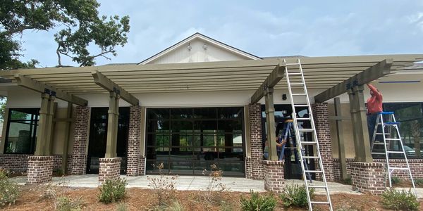 Workers install a large pergola on a brick patio outside a modern house.
