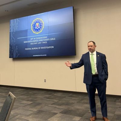 Man in suit giving presentation on FBI Sandworm investigation.