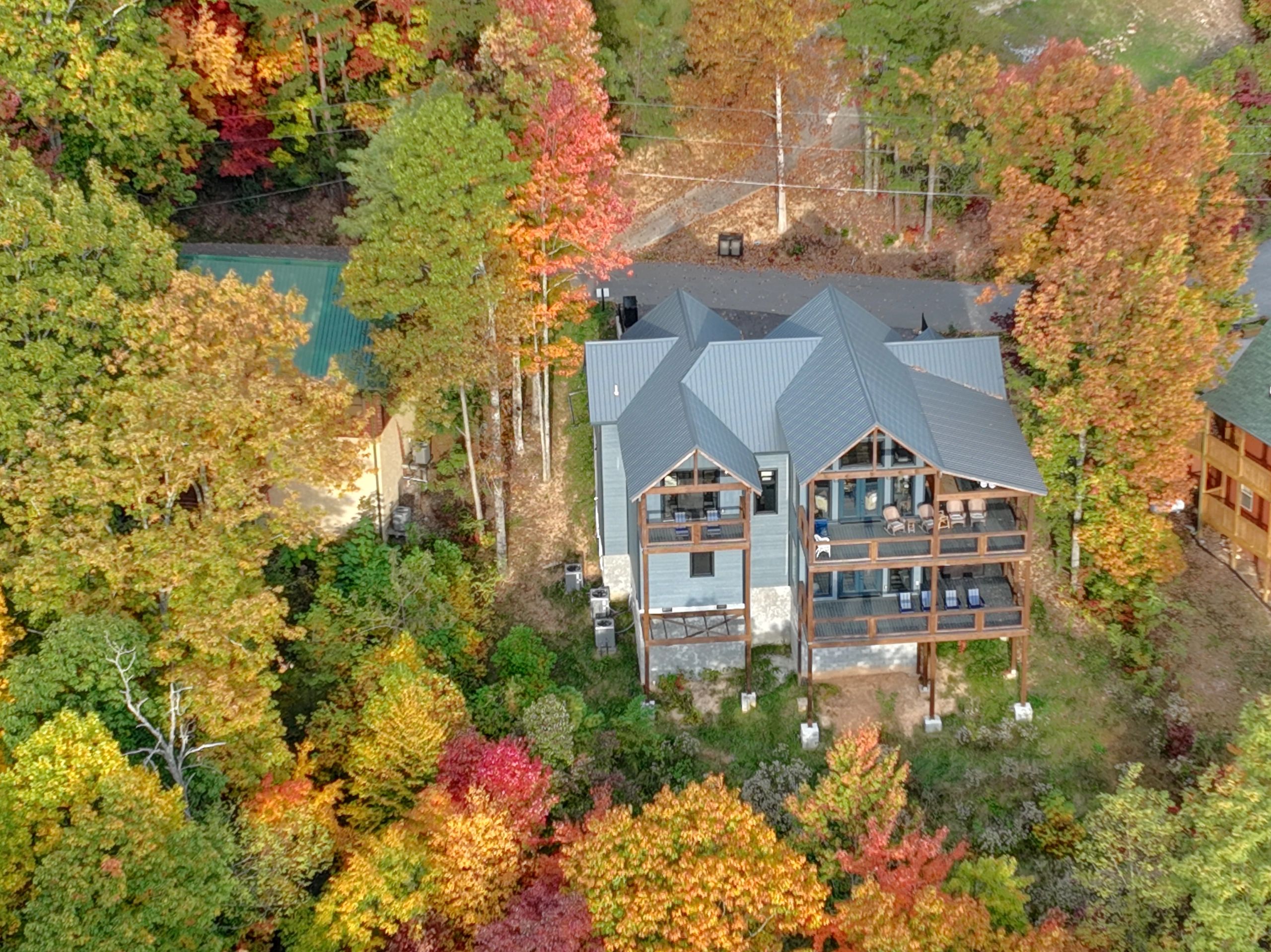 Aerial view of a modern cabin surrounded by colorful autumn trees.