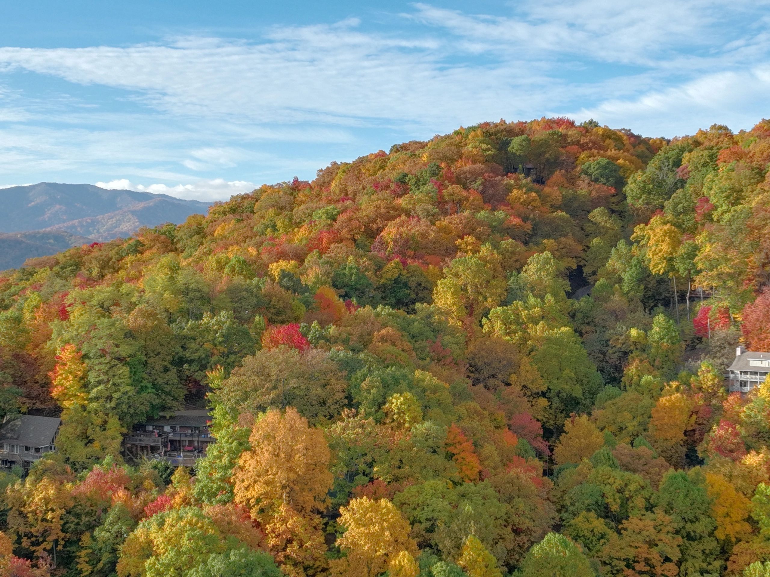 Colorful autumn foliage covering rolling hills under a partly cloudy sky.
