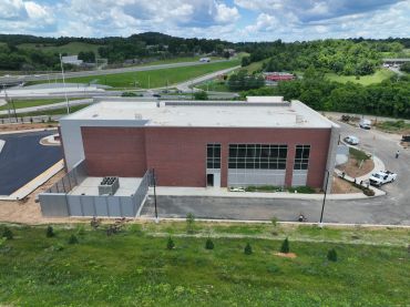 A modern commercial building under construction with a green landscape.