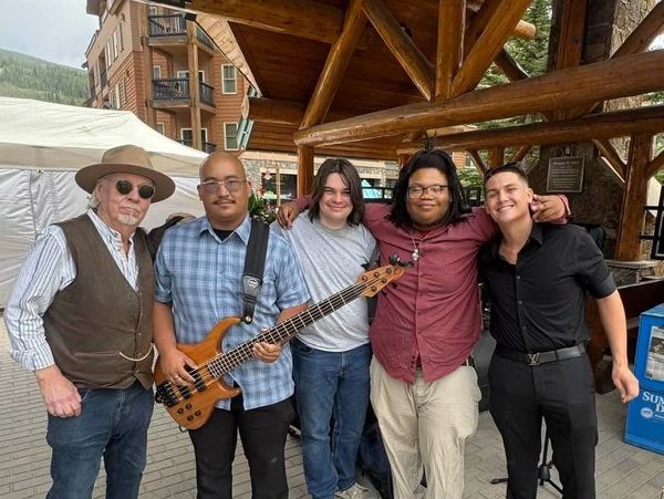 Group of five musicians posing together outdoors.