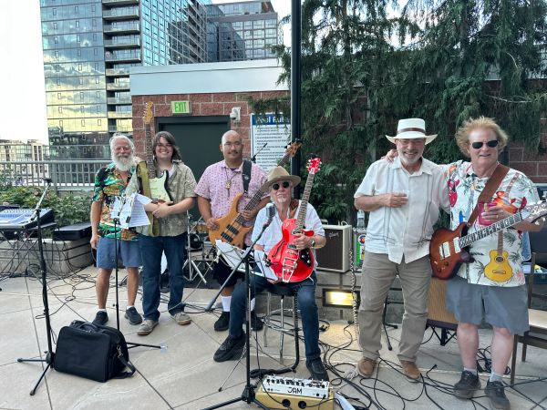 Group of six musicians posing with instruments on an outdoor stage.