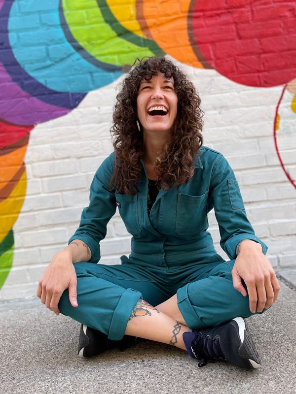 Jenny sitting on ground laughing in front
Of colorful painted mural