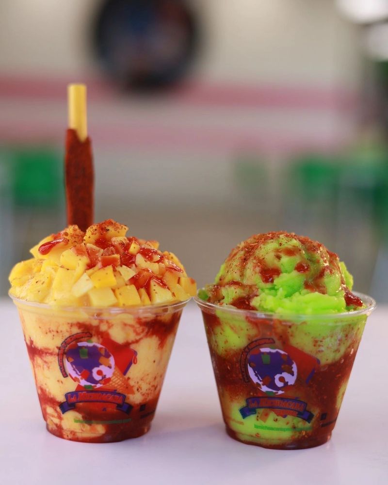 Two colorful fruit-flavored shaved ice cups with chili powder and sauce.