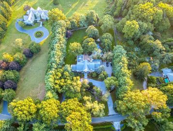 Aerial view of two houses surrounded by lush green trees and lawns.
