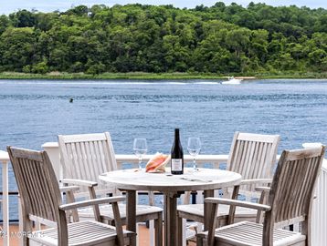 Outdoor wooden table with chairs overlooking a lake and forested shore.