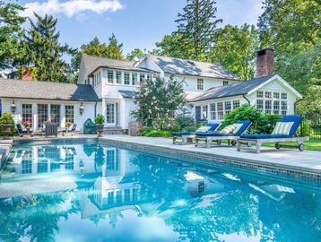 Elegant white house with a clear blue swimming pool and lounge chairs.