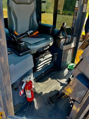 Interior view of a construction vehicle cabin with controls and a fire extinguisher.