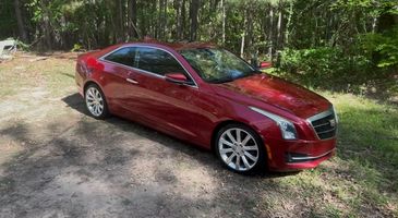 Red Cadillac parked on a dirt path surrounded by trees.