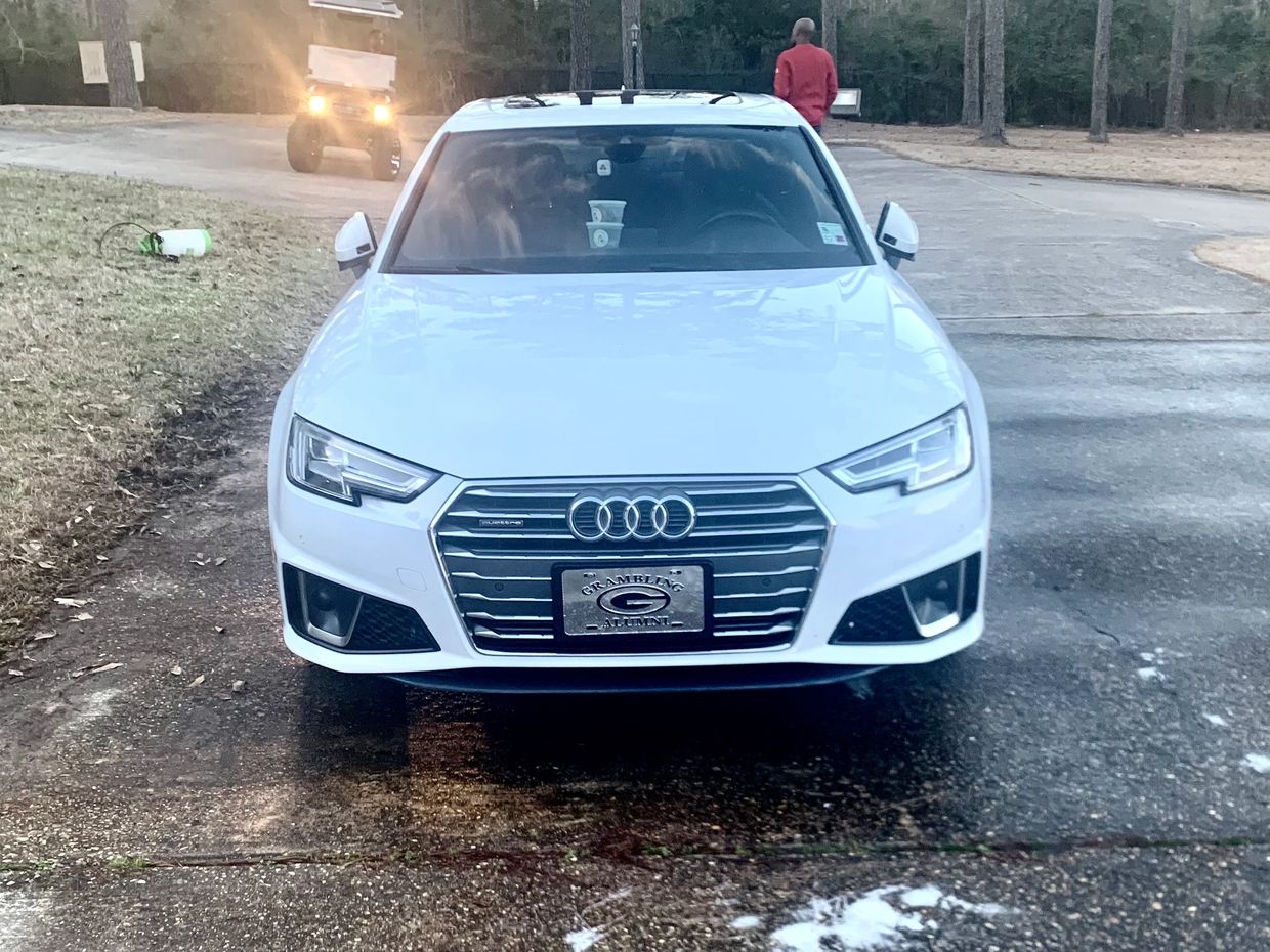 Front view of a white Audi car parked on a driveway with a person walking in the background.