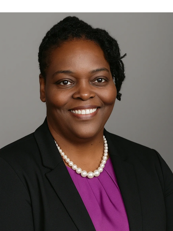 Professional woman in a black blazer and pearl necklace smiling warmly.